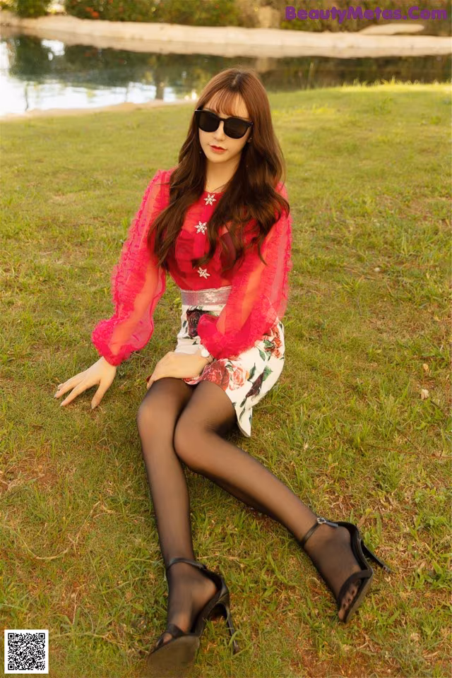 A woman sitting on the grass wearing a pink blouse and black tights.