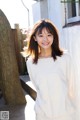 A woman in a white sweatshirt standing next to a tree.