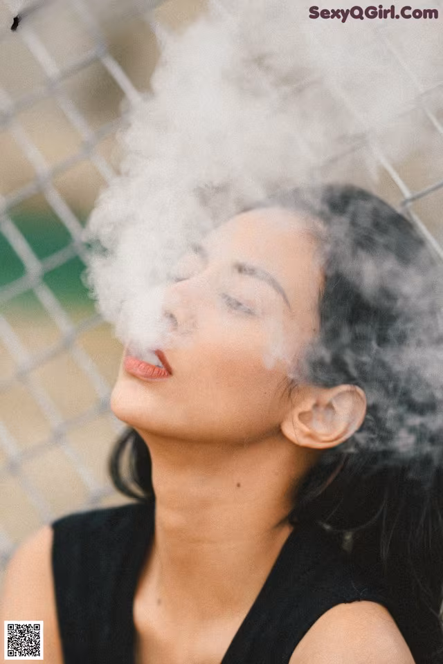 A woman is smoking a cigarette in front of a fence.