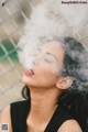 A woman is smoking a cigarette in front of a fence.