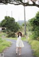 A woman in a white dress and straw hat walking down a road.