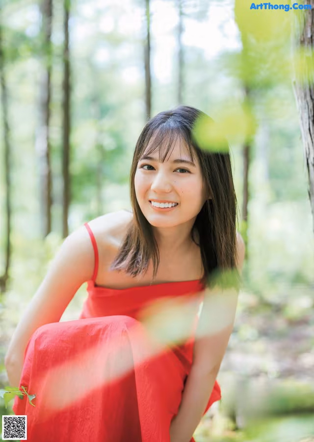 A woman in a red dress sitting in the woods.