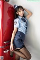 A woman in a police uniform leaning against a red refrigerator.